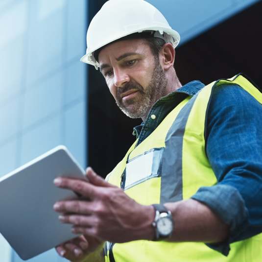 Time tracking software in constructionn: Those who rely on Insite LMS have times, accesses, certificates and reports under control. Site manager in high-visibility vest and white helmet looks at his tablet on the construction site.